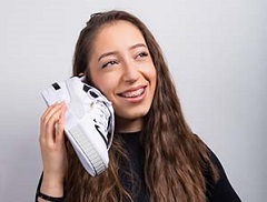 Mädchen hält sich weißen Sneaker mit schwarzen Details wie einen Telefonhörer an die Wange