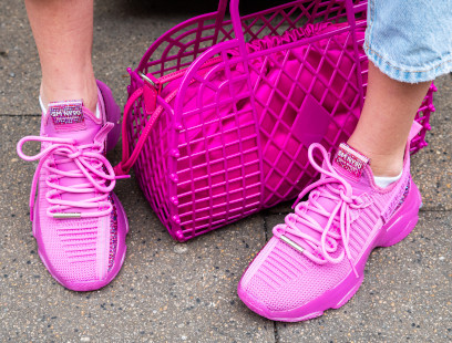 Die Füße einer Frau, die pinke Steve Madden-Sneaker trägt. Daneben eine dazu passende, pinke Tasche.